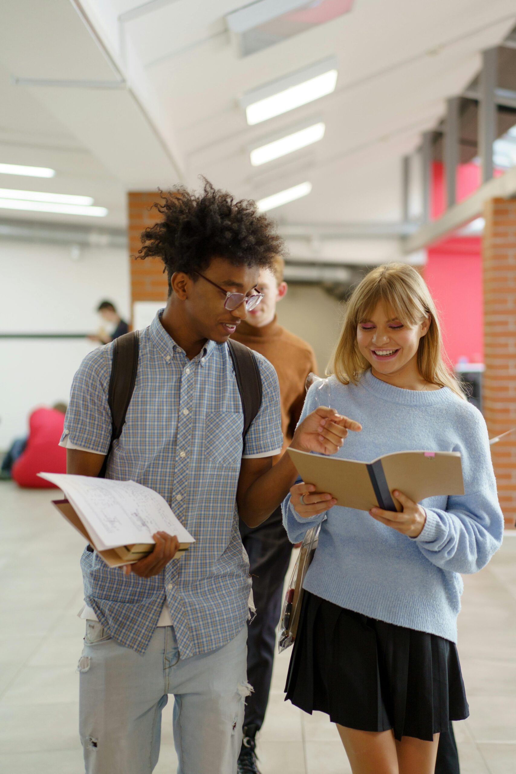 Cheerful students discuss in a university hallway, engaging with notebooks and learning materials.